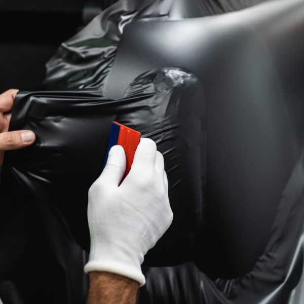 Car wrapping specialist putting vinyl foil or film on car. Selective focus.