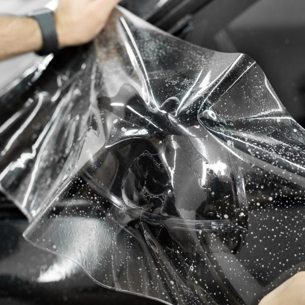 Man applying sticking protective film on a car mirror at the vehicle service station. Detailing studio.